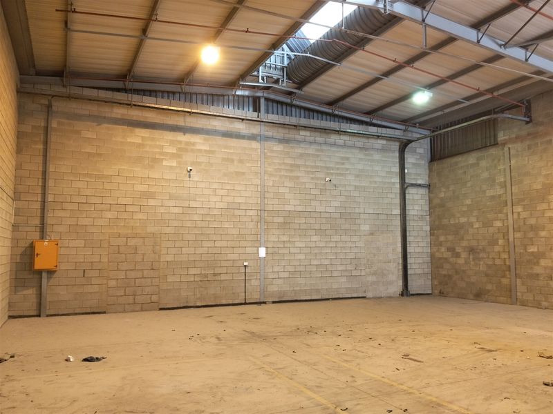 Spacious industrial warehouse unit featuring high ceilings with exposed steel trusses, concrete block walls, concrete flooring, and integrated fire sprinkler system.