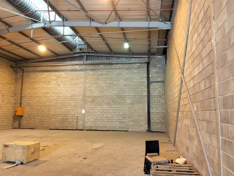 Spacious industrial warehouse unit featuring high ceilings with exposed steel trusses, concrete block walls, and functional industrial lighting.