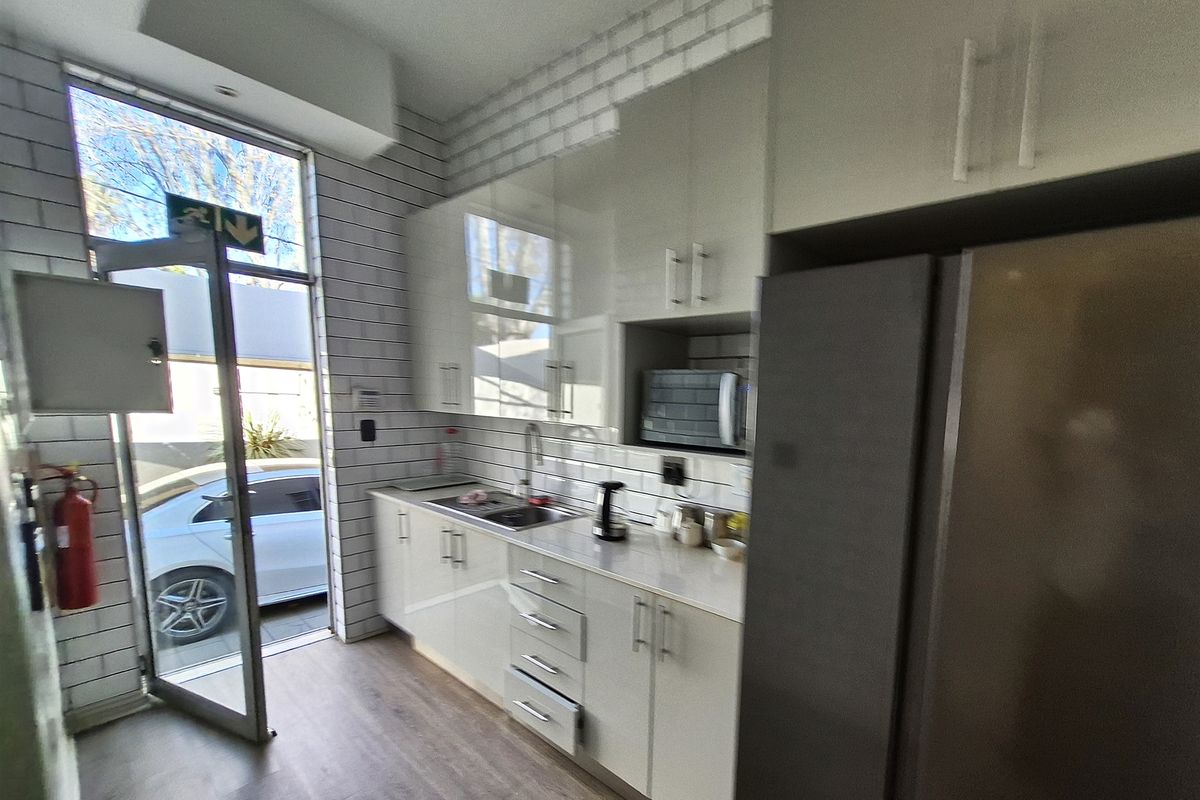 A modern office kitchenette featuring white high-gloss cabinetry, subway tile backsplash, stainless steel sink, and direct access to the exterior.