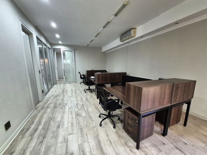 A modern office space featuring wood-look laminate flooring, glass partitions, and integrated air conditioning, providing a professional and functional work environment.