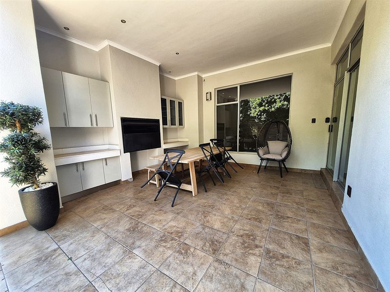Covered patio area featuring tiled flooring, built-in cabinetry with stone countertops, and a built-in braai, ideal for outdoor entertaining.