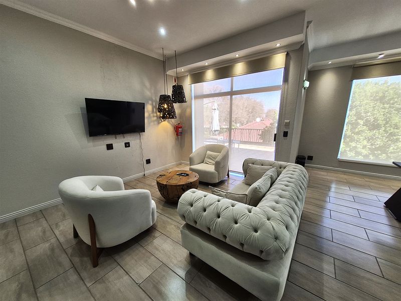 A modern office lounge area featuring tiled flooring, recessed lighting, and large sliding glass doors providing natural light and access to an outdoor balcony.