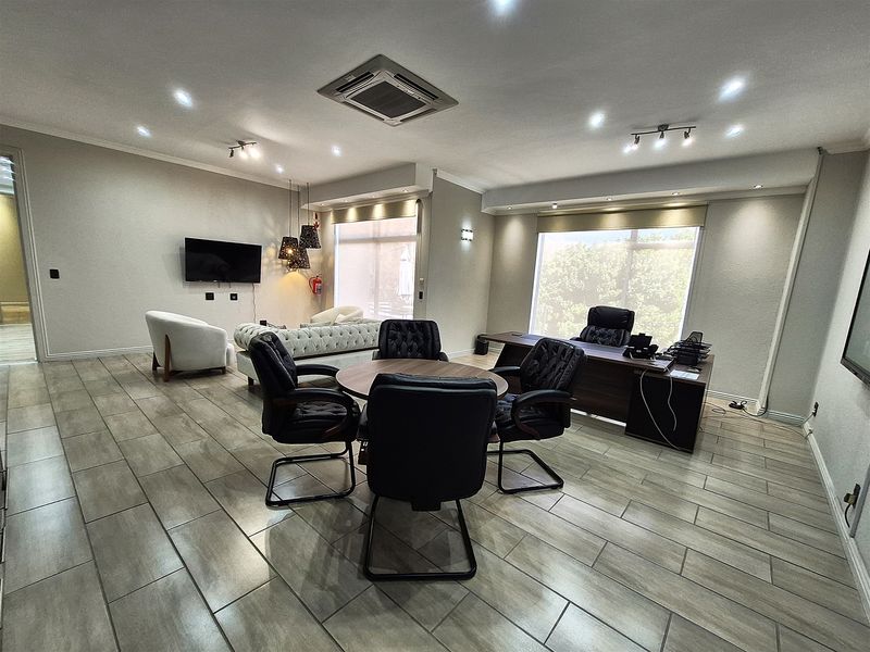 A spacious, well-lit professional office featuring modern tiled flooring, recessed ceiling lights, a built-in cassette air conditioning unit, and large windows with roller blinds.