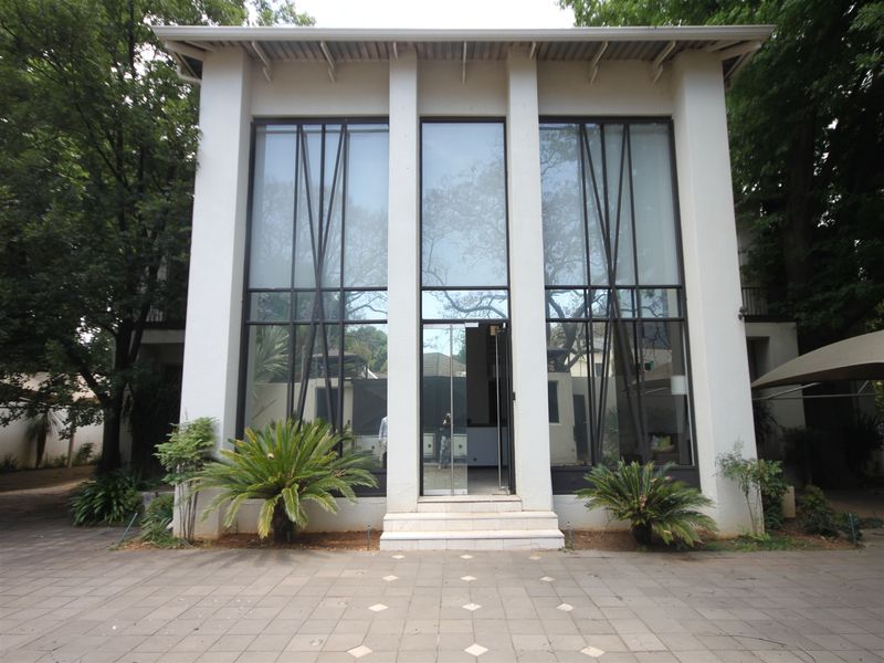 A modern office building entrance featuring a striking full-height glass facade with geometric metal detailing and a paved approach.