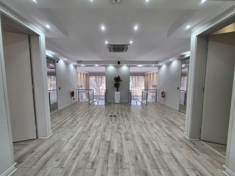 A modern, spacious office hallway featuring laminate wood flooring, recessed lighting, and glass balustrades leading to an open landing area.