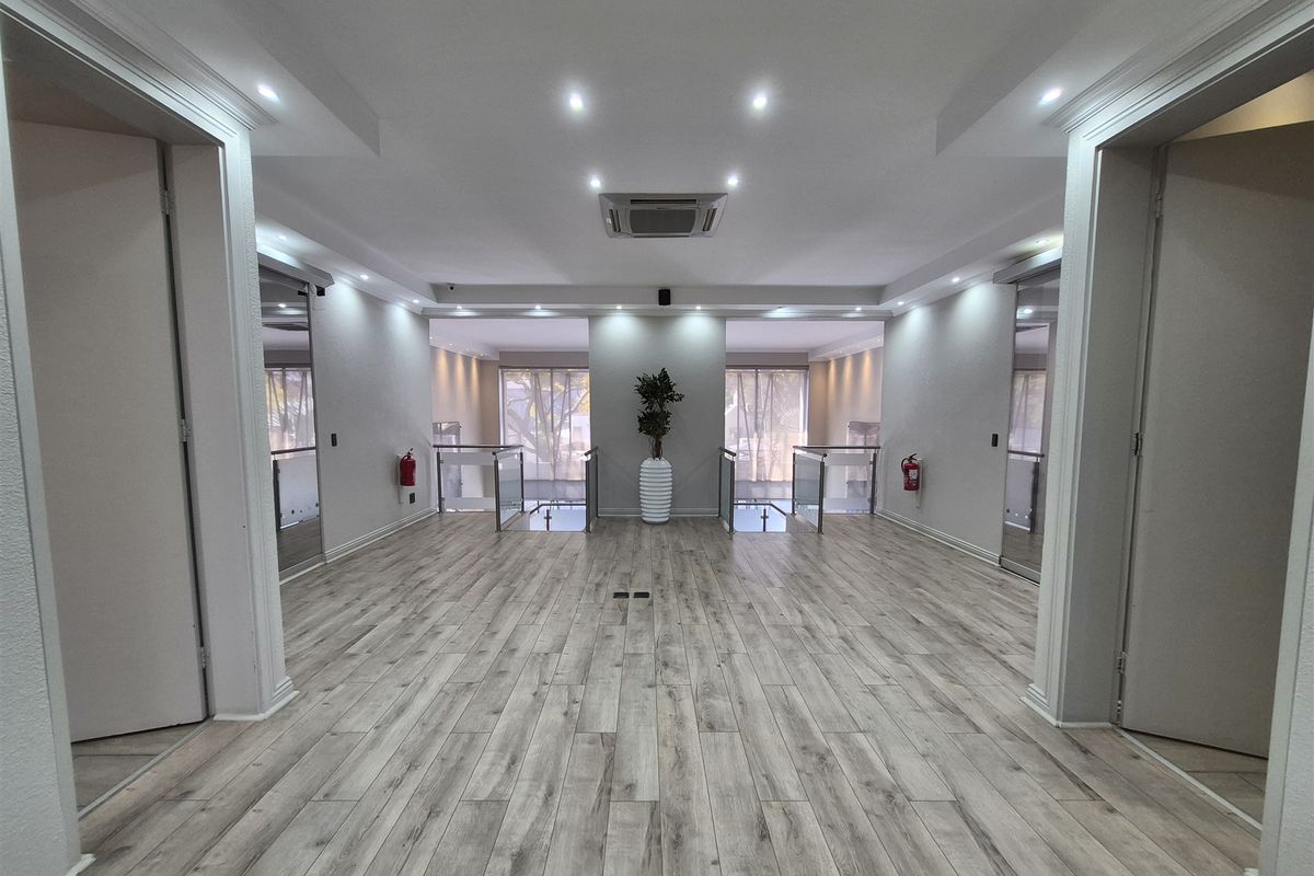 A modern, spacious office hallway featuring laminate wood flooring, recessed lighting, and glass balustrades leading to an open landing area.