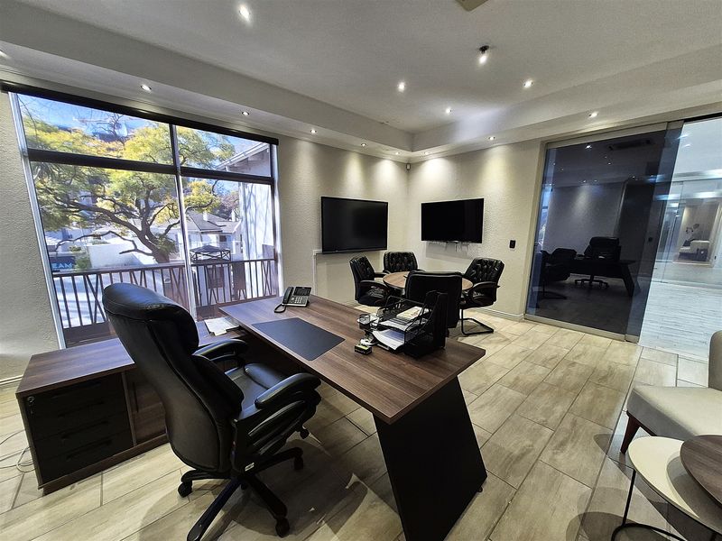 A professional office space featuring modern tiled flooring, recessed lighting, large windows with natural light, and a glass partition wall.