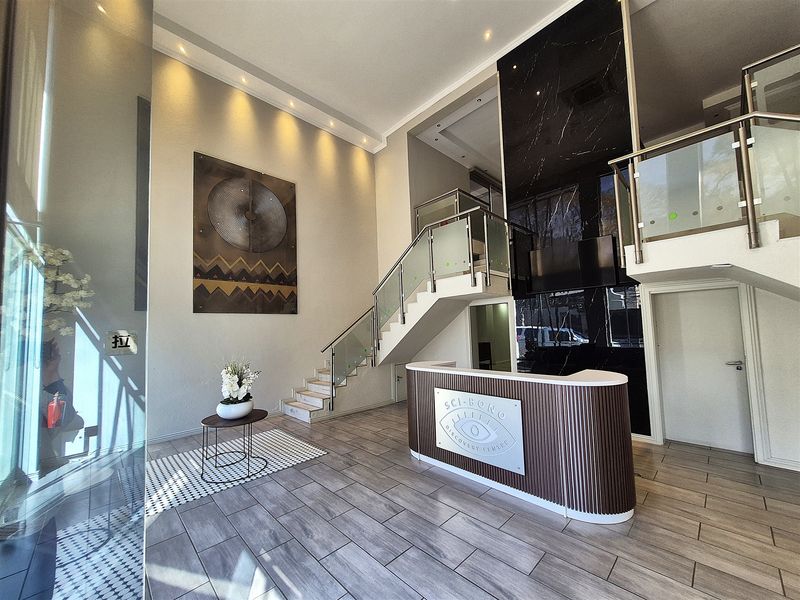 Modern office reception area featuring a sleek reception desk, marble accent wall, and a contemporary staircase with glass balustrades.