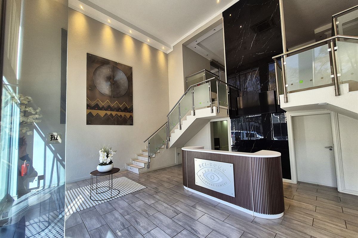 Modern office reception area featuring a sleek reception desk, marble accent wall, and a contemporary staircase with glass balustrades.