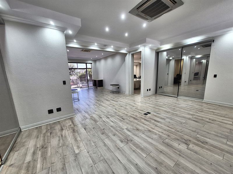 Spacious, modern office area featuring wood-look laminate flooring, recessed ceiling lighting, integrated air conditioning, and large mirrored storage doors.