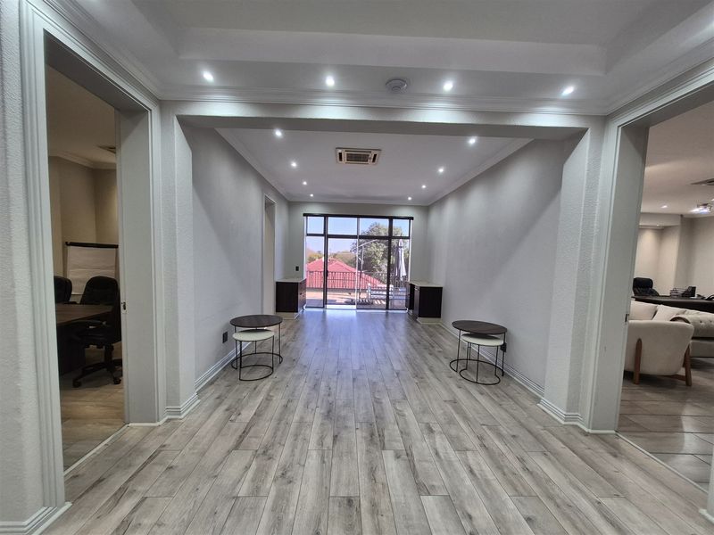 A bright, open-plan office space featuring modern laminate flooring, recessed ceiling lighting, and built-in cabinetry with access to an outdoor balcony.