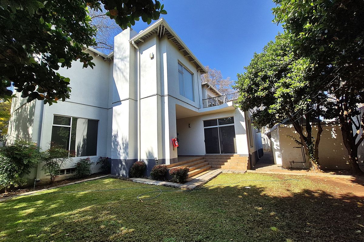 Rear view of the office property featuring a landscaped garden, tiled patio area, balcony, and large sliding glass doors providing access to the building.