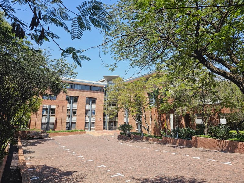 A professional office building featuring a classic red brick facade, large glass entrance, and a paved driveway surrounded by mature trees.