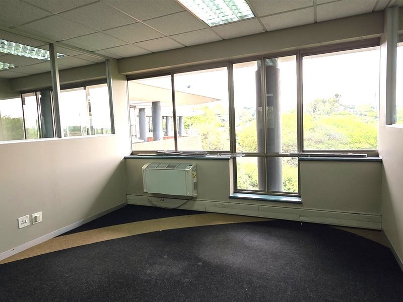 A vacant office space featuring large windows, glass partitions, a wall-mounted HVAC unit, and a suspended ceiling with recessed lighting.