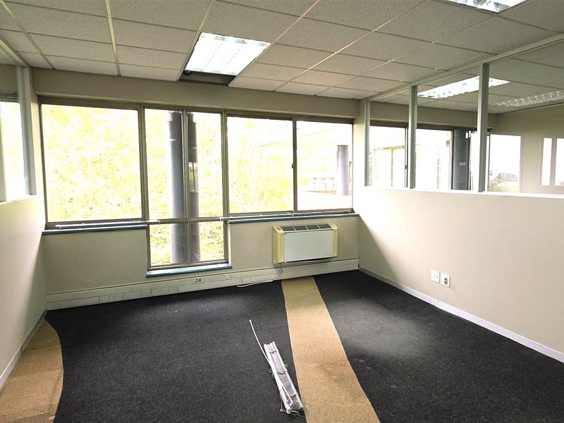 Empty office space featuring glass partitions, suspended ceilings, and an integrated HVAC unit, requiring flooring updates.