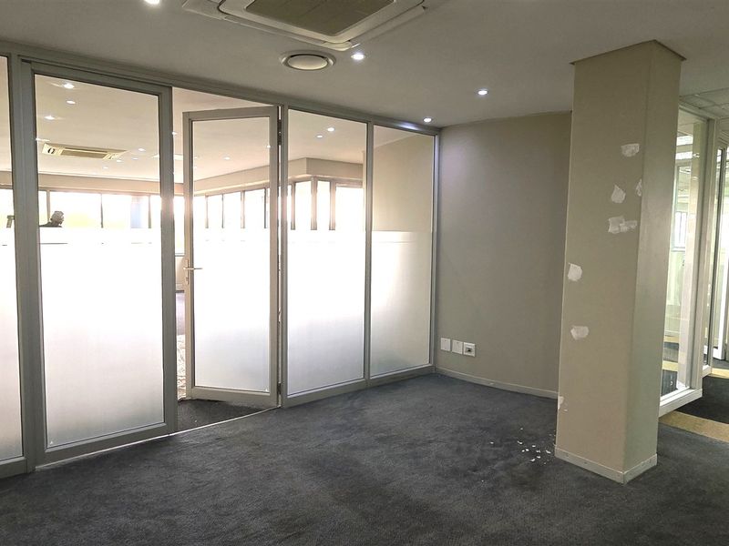 Empty office space featuring glass partition walls, recessed lighting, and carpeted flooring, suitable for a professional workspace layout.