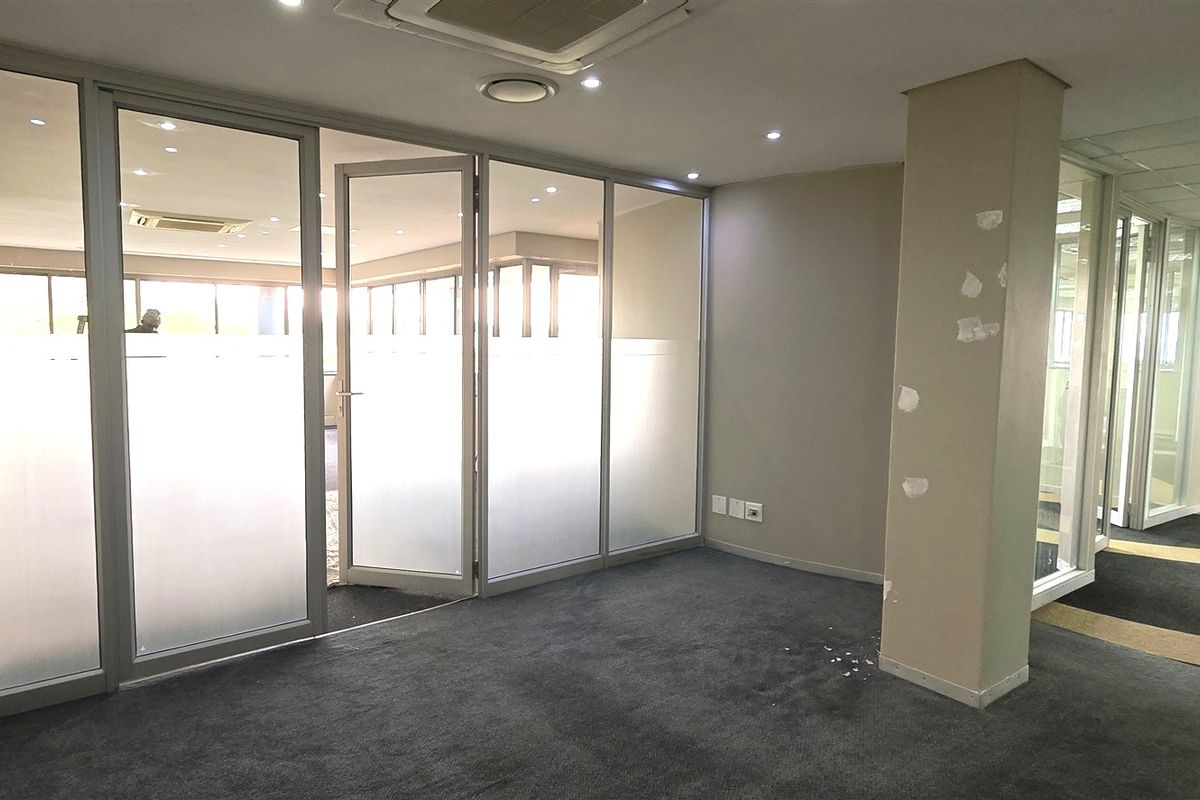 Empty office space featuring glass partition walls, recessed lighting, and carpeted flooring, suitable for a professional workspace layout.
