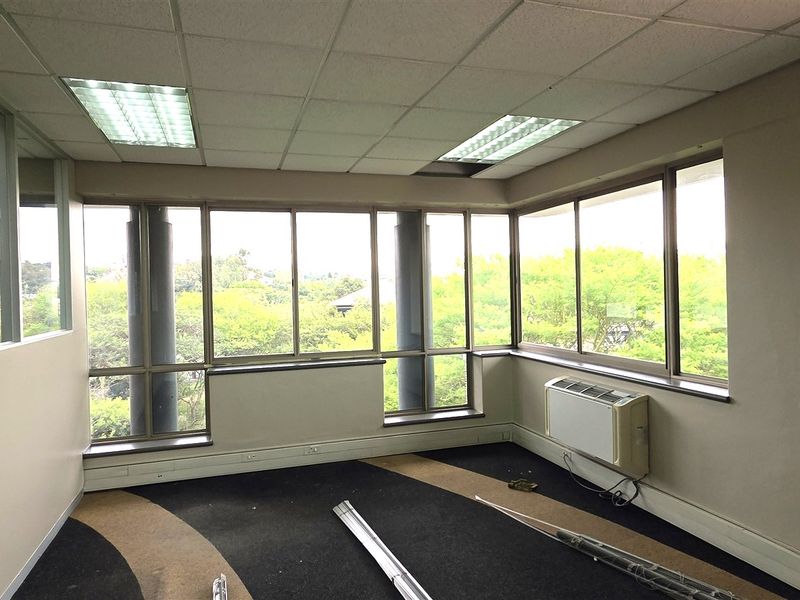 An empty office space featuring large windows with natural light, suspended ceilings, recessed lighting, and a wall-mounted HVAC unit.