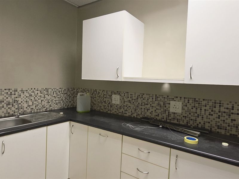 A functional kitchenette area featuring white cabinetry, dark laminate countertops, and a mosaic tile backsplash with a stainless steel sink.