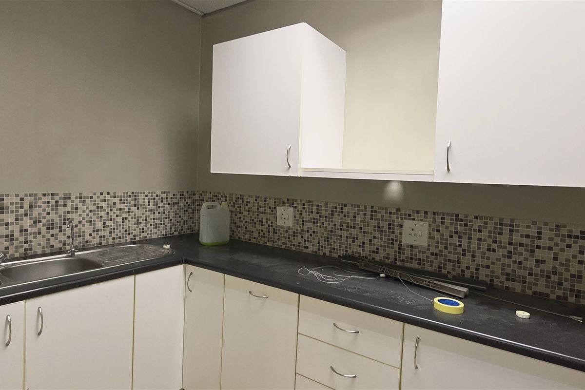A functional kitchenette area featuring white cabinetry, dark laminate countertops, and a mosaic tile backsplash with a stainless steel sink.