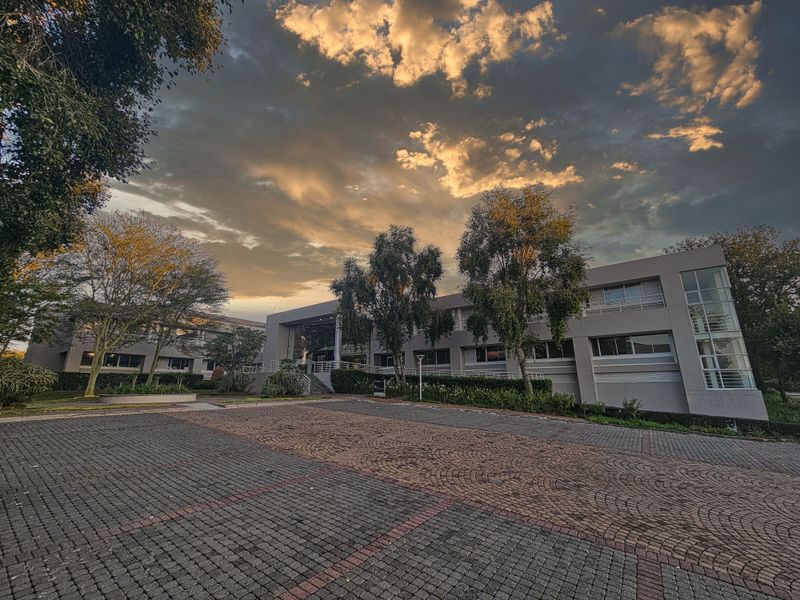 A professional exterior view of a multi-story office building featuring a paved driveway and landscaped grounds under a dramatic sunset sky.