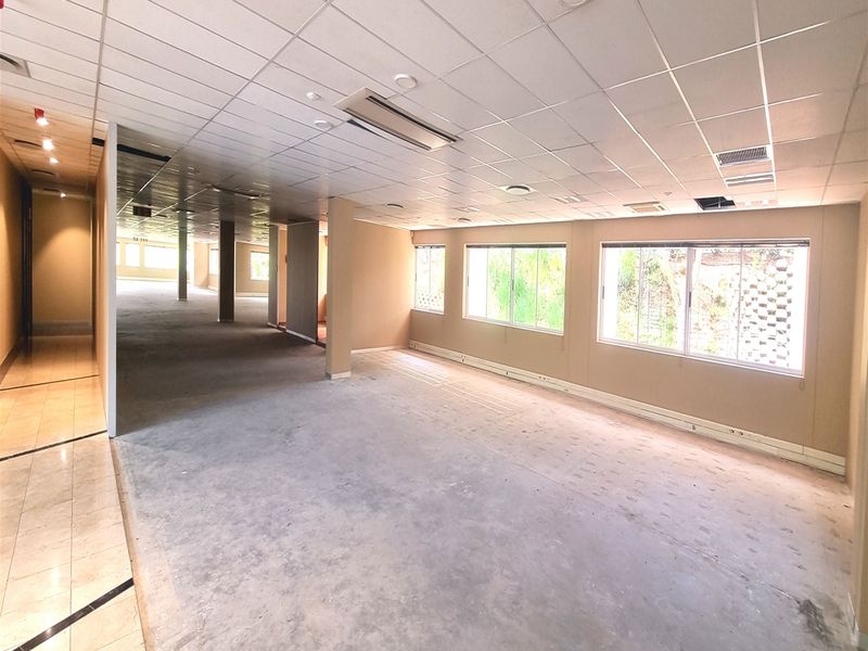 A large, vacant open-plan office space featuring a suspended ceiling, recessed lighting, ducted air conditioning, and expansive windows providing natural light.