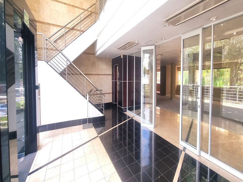 Modern office building entrance lobby featuring a grand staircase, glass partitions, and high-quality tiled flooring with recessed lighting.