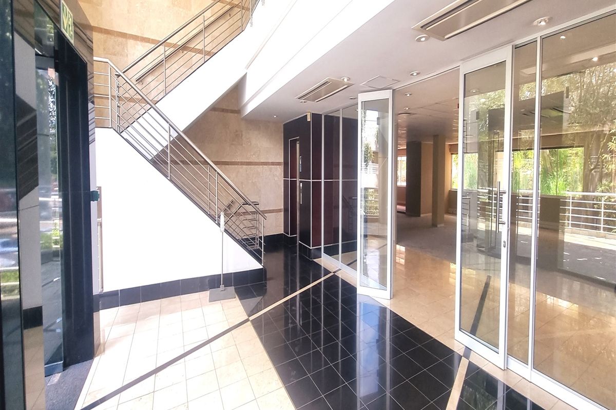 Modern office building entrance lobby featuring a grand staircase, glass partitions, and high-quality tiled flooring with recessed lighting.