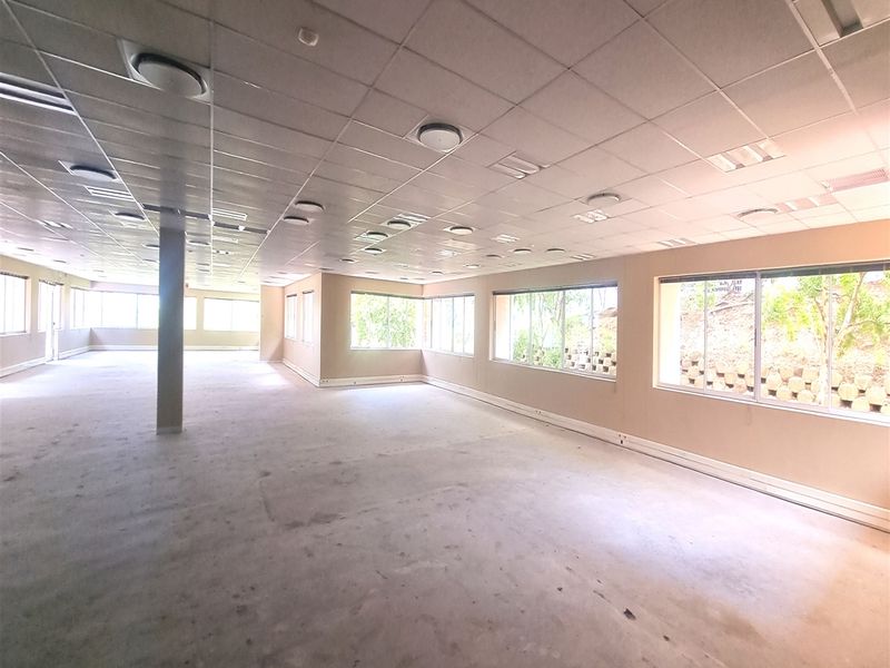 A spacious, open-plan office area featuring a suspended ceiling, recessed lighting, and large windows providing ample natural light.
