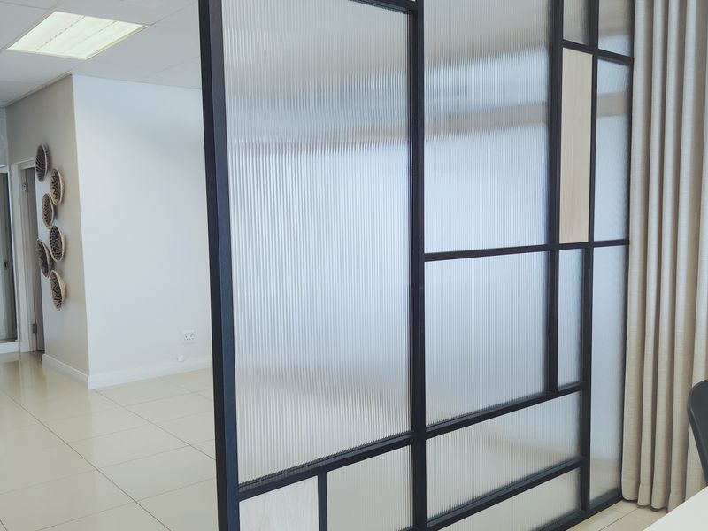Modern office space featuring a contemporary black-framed fluted glass partition, tiled flooring, and recessed ceiling lighting.