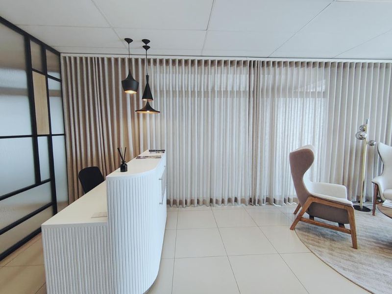A modern office reception area featuring a sleek curved white desk, tiled flooring, and floor-to-ceiling curtains providing a professional and welcoming atmosphere.