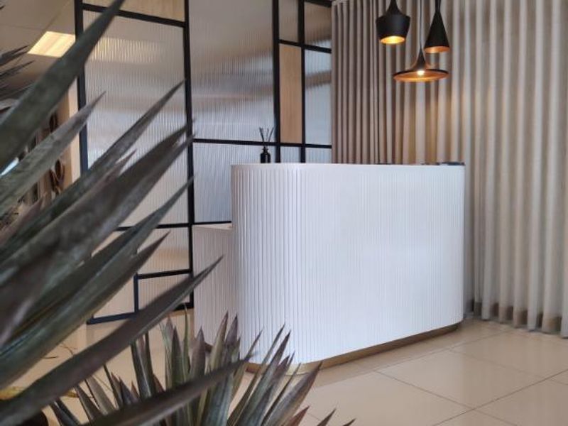 Modern professional reception area featuring a sleek fluted white desk, contemporary pendant lighting, and a stylish glass and metal partition screen.