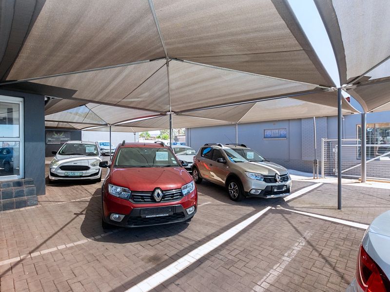 A paved outdoor vehicle display area featuring a large shade cloth canopy structure and direct access to the retail storefront.