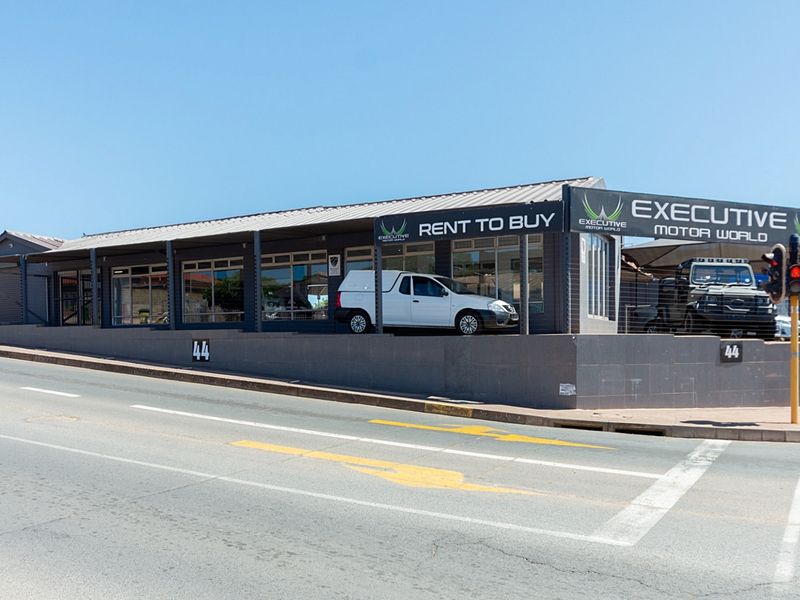 Street-level view of a commercial retail property featuring a metal roof, large glass storefront windows, and prominent signage on a corner lot.