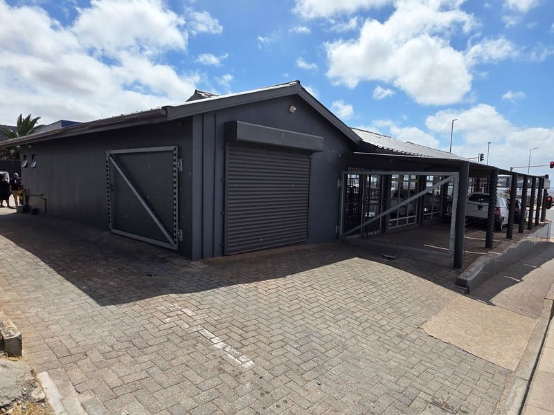 Exterior view of a commercial retail property featuring a dark grey facade, roller shutter security doors, and a paved frontage.