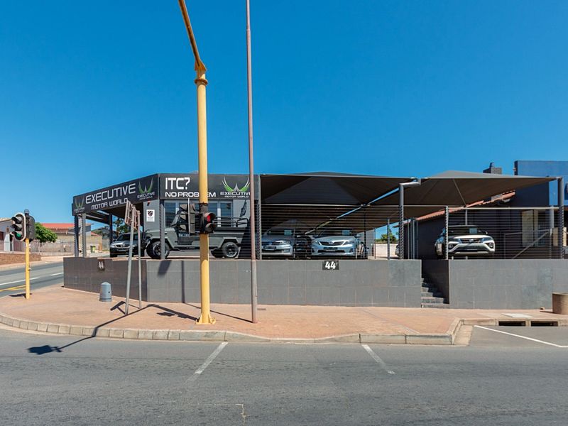 Street-level view of a commercial retail property featuring a paved forecourt, shade cloth canopy, and tiled retaining wall.