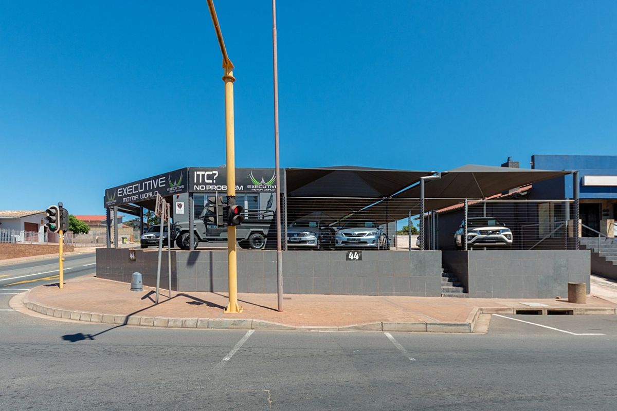 Street-level view of a commercial retail property featuring a paved forecourt, shade cloth canopy, and tiled retaining wall.