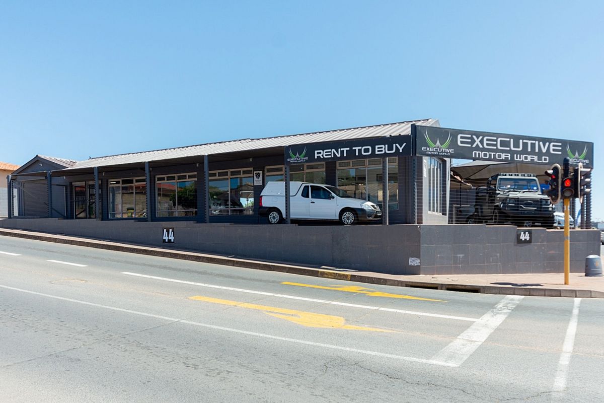 Street-level view of a commercial retail property featuring a metal roof, large glass storefront windows, and prominent signage on a corner lot.