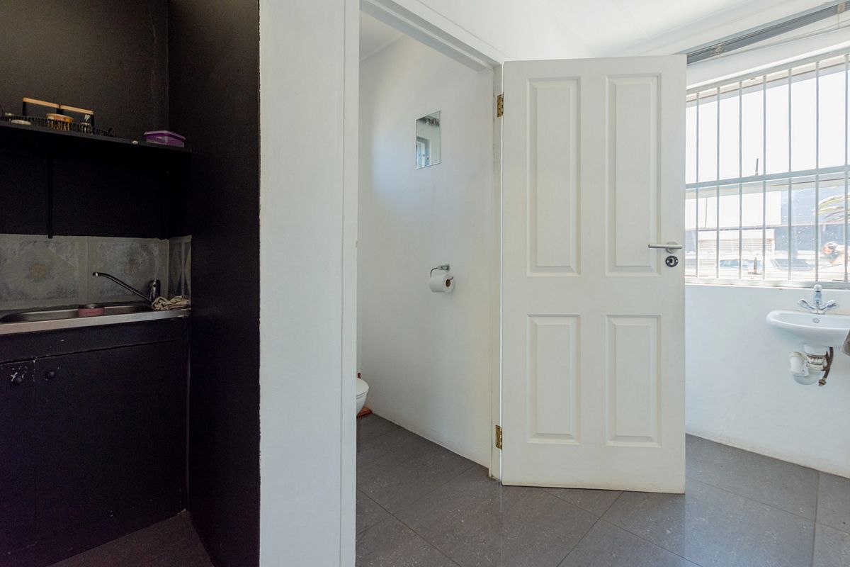 A functional bathroom area featuring a wall-mounted basin, tiled flooring, and a separate toilet cubicle with a secure window.