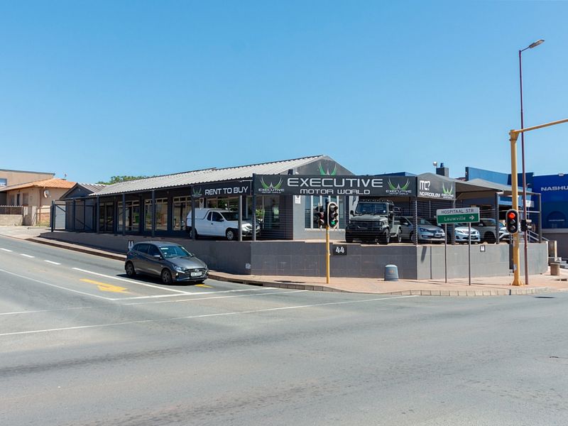 Street-level view of a commercial retail property featuring a metal roof, tiled facade, and large display windows, situated on a corner lot.