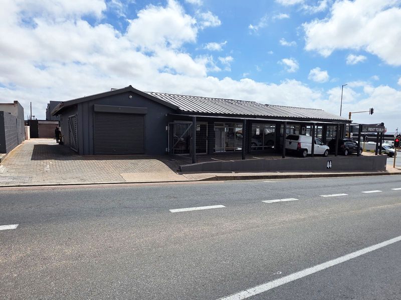 Street-facing commercial property featuring a modern dark facade, metal roofing, secure roller shutter access, and a paved frontage area.