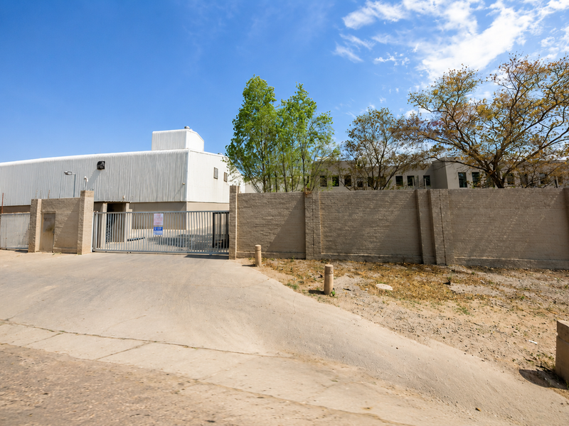 Industrial property exterior featuring a corrugated metal warehouse structure, secure perimeter brick walling, and a gated concrete driveway entrance.