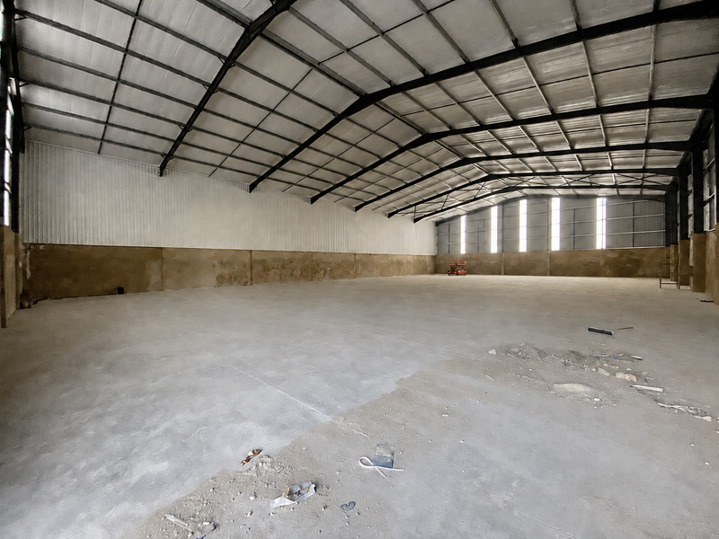 Large industrial warehouse space featuring a high-clearance steel portal frame, concrete flooring, and metal wall cladding, suitable for storage or manufacturing operations.