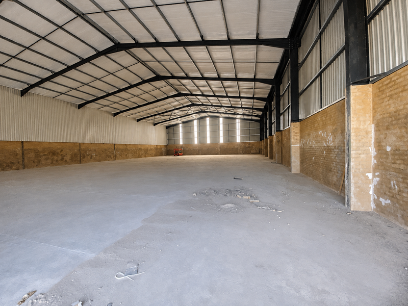 Spacious industrial warehouse featuring a high-clearance steel portal frame, exposed brick walls, and durable concrete flooring, suitable for various commercial or storage applications.