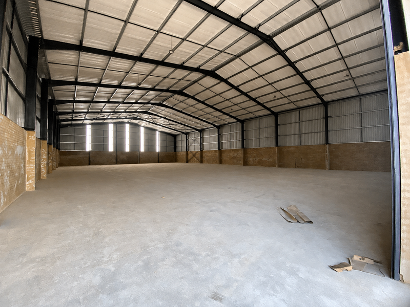 Spacious industrial warehouse featuring a high-clearance steel portal frame, corrugated metal roofing, and durable concrete flooring, suitable for storage or manufacturing operations.