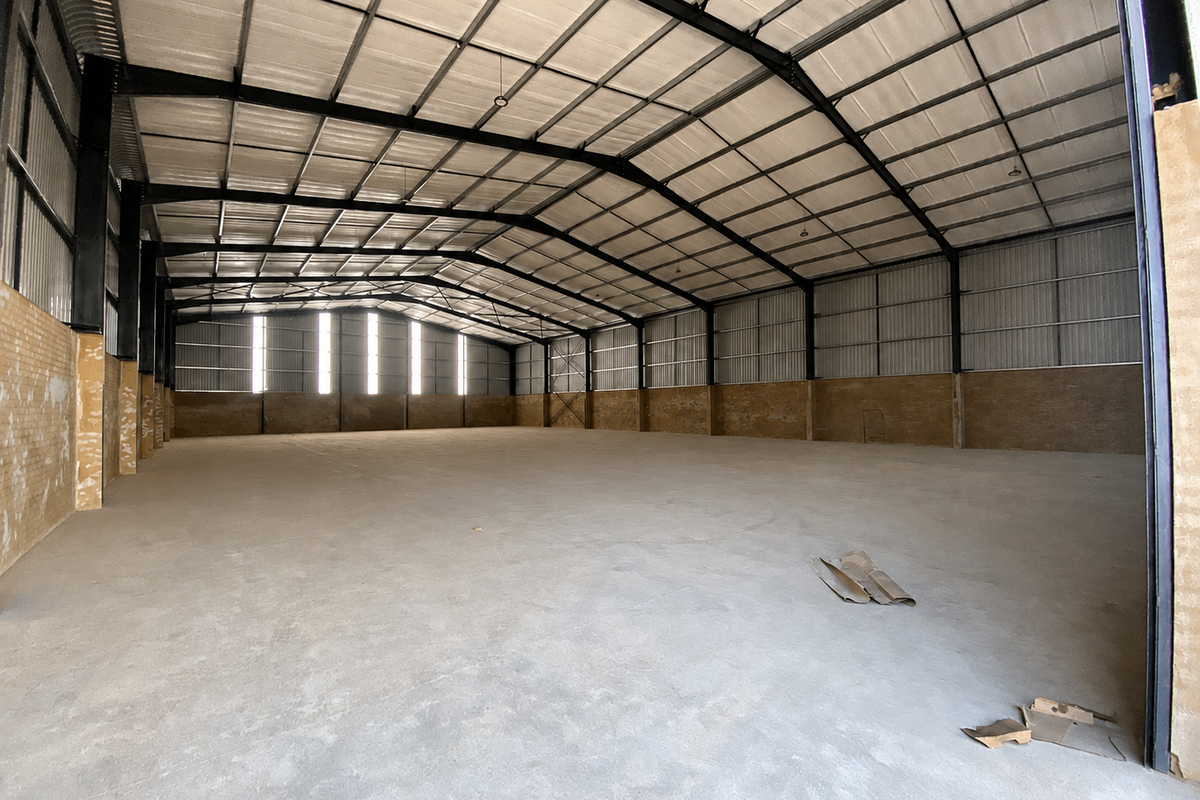 Spacious industrial warehouse featuring a high-clearance steel portal frame, corrugated metal roofing, and durable concrete flooring, suitable for storage or manufacturing operations.
