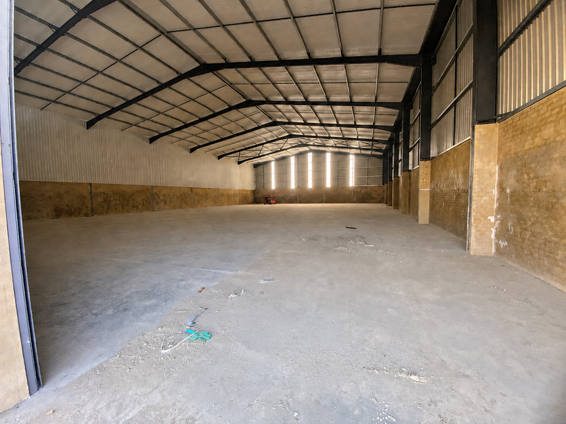 Spacious industrial warehouse unit featuring a high-clearance steel portal frame, concrete flooring, and brick masonry walls with natural light from clerestory windows.
