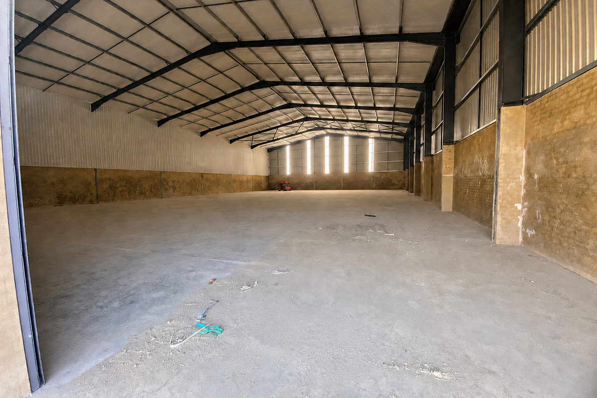 Spacious industrial warehouse unit featuring a high-clearance steel portal frame, concrete flooring, and brick masonry walls with natural light from clerestory windows.