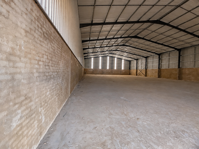 Spacious industrial warehouse featuring a high-clearance steel portal frame, concrete flooring, and brick masonry walls with natural light from translucent roof panels.