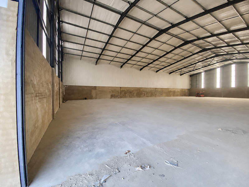 Spacious industrial warehouse featuring high ceilings with exposed steel trusses, concrete flooring, and metal wall cladding, suitable for storage or manufacturing operations.